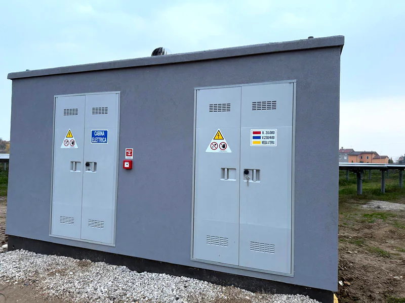 Cabina elettrica prefabbricata con due porte doppie, accanto alle strutture di un impianto fotovoltaico